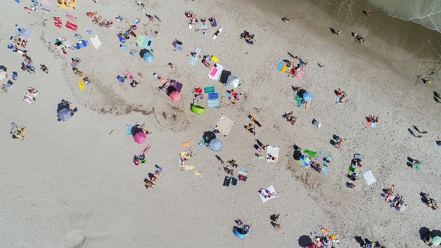 Aerial view of a crowded white sand beach with many umbrellas and people, contrasted with a quieter section further down. (good beaches in usa)